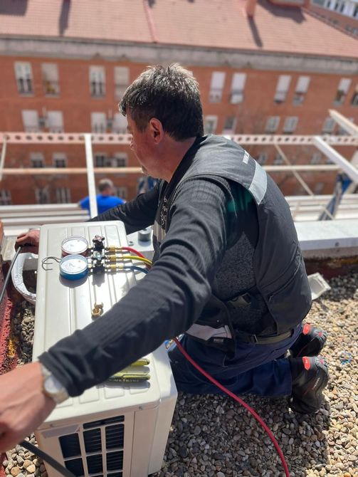 Un hombre está trabajando en un aire acondicionado en una azotea.