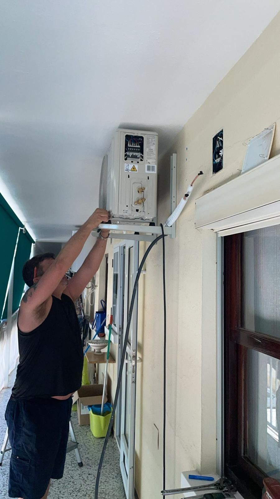 Un hombre está instalando un aire acondicionado en un balcón.