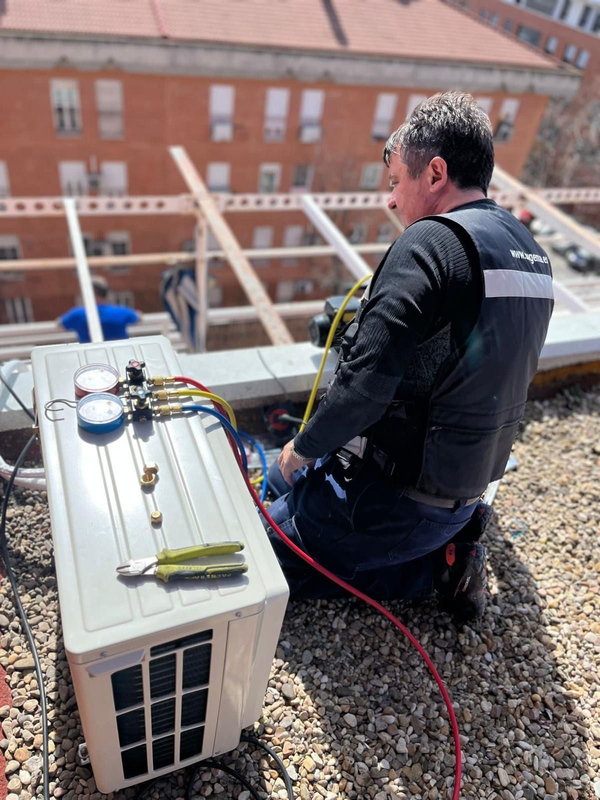 Un hombre está arrodillado en un tejado trabajando en un aire acondicionado.